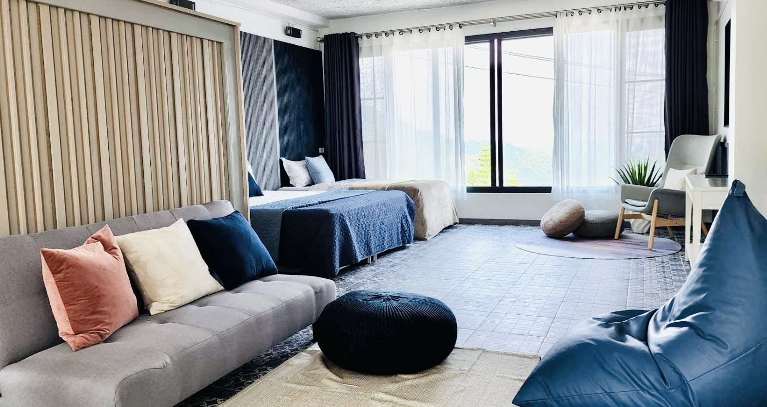 Family Deluxe ground floor with two beds, a grey sofa with pastel pillows, and floor-to-ceiling windows looking out over the mountains.